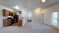 This single-floor residential unit offers a well-designed, functional layout that balances open communal spaces with private retreats. The living area is immediately welcoming, highlighted by dramatic vaulted ceilings that amplify the sense of space, plush neutral carpeting, and a ceiling fan with light fixture. Pendant lighting connects the living area to the adjoining kitchen, which is equipped with black appliances including a refrigerator, range, microwave, and dishwasher, set against warm honey-toned cabinetry and granite-style countertops. Wood-look flooring runs throughout the kitchen, which also provides direct access to an in-unit laundry area housing a full-size washer. A dedicated entry foyer with hardwood-style flooring greets residents at the front door. Multiple bedrooms feature plush carpeting, ceiling fans, and windows with blinds that invite natural light. Walk-in closet storage is available in at least one bedroom. Both bathrooms are finished consistently with warm wood cabinetry, granite-style countertops, dual sinks in one bath, and a tub-shower combination with a curved curtain rod. Wood-look flooring completes the bathroom finishes, creating a cohesive and clean aesthetic throughout the unit.
