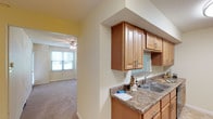 This single-floor residence offers a thoughtfully designed layout that balances comfort and functionality. The galley-style kitchen is a standout feature, lined on both sides with warm honey-toned wood cabinetry offering generous storage space. Granite-look countertops provide ample prep surface, while black appliances — including a range, built-in microwave, and dishwasher — lend a sleek contrast. A double-basin stainless steel sink and tile flooring complete the practical yet attractive kitchen space.

Adjacent living and bedroom areas are finished with plush wall-to-wall carpeting, creating a comfortable, cozy atmosphere. Ceiling fans with light fixtures are present throughout, ensuring year-round comfort and consistent airflow. Soft yellow-toned walls add a warm, inviting character to the interior.

Natural light flows generously through multiple windows fitted with blinds for privacy and light control. A set of sliding glass doors in one of the main rooms opens directly to a lush outdoor green space, seamlessly connecting the interior to the exterior. An additional room features a door and dual windows, offering versatility as a bedroom or flex space.

The bathroom is clean and neutral, featuring textured walls and dual towel bars, maintaining the home's overall sense of practicality and ease. Throughout the space, the design prioritizes livability with a bright, airy ambiance.
