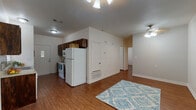 This single-story residence offers a practical and comfortable layout with warm hardwood-style flooring that flows consistently throughout every room. The open living and dining area is bright and welcoming, featuring a ceiling fan with light fixture and neutral white walls that create a clean, airy atmosphere. Natural light enters through windows fitted with white blinds, adding to the overall sense of openness.

The galley-style kitchen is efficiently designed, showcasing rich dark wood cabinetry, light stone-finish countertops, and a mosaic tile backsplash that adds a decorative touch. White appliances — including a refrigerator, electric range, microwave, and dishwasher — are included. A rear entry door with a windowed panel provides additional access and natural light to the kitchen.

The residence includes multiple bedrooms, each equipped with a ceiling fan and light fixture. One bedroom features a spacious walk-in closet with built-in shelving and hanging rods, while another benefits from a window with outdoor views. The bathroom is well-appointed with a wide vanity featuring dark wood cabinetry, a light countertop, a large mirror with overhead lighting, and a combination tub and shower. The consistent flooring and neutral color palette throughout create a cohesive and move-in-ready living environment.