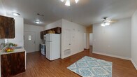 This single-story residence offers a practical and comfortable layout with warm hardwood-style flooring that flows consistently throughout every room. The open living and dining area is bright and welcoming, featuring a ceiling fan with light fixture and neutral white walls that create a clean, airy atmosphere. Natural light enters through windows fitted with white blinds, adding to the overall sense of openness.

The galley-style kitchen is efficiently designed, showcasing rich dark wood cabinetry, light stone-finish countertops, and a mosaic tile backsplash that adds a decorative touch. White appliances — including a refrigerator, electric range, microwave, and dishwasher — are included. A rear entry door with a windowed panel provides additional access and natural light to the kitchen.

The residence includes multiple bedrooms, each equipped with a ceiling fan and light fixture. One bedroom features a spacious walk-in closet with built-in shelving and hanging rods, while another benefits from a window with outdoor views. The bathroom is well-appointed with a wide vanity featuring dark wood cabinetry, a light countertop, a large mirror with overhead lighting, and a combination tub and shower. The consistent flooring and neutral color palette throughout create a cohesive and move-in-ready living environment.