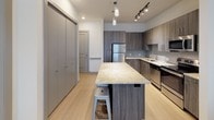 Located at 115 N Mesquite St in Arlington, TX, this single-floor unit features a contemporary open-concept design with clean lines and modern finishes throughout. The kitchen serves as a central highlight, showcasing dark wood-grain cabinetry that extends floor-to-ceiling for ample storage, light granite countertops, a subway tile backsplash, and stainless steel appliances including a full-size refrigerator and range. A spacious kitchen island with seating provides an ideal space for dining or casual gatherings, while pendant lighting and a track light fixture illuminate the space effectively. Light wood-style flooring runs through the kitchen and living areas, creating a cohesive, contemporary aesthetic. The living area offers natural light through slatted blinds, contributing to a bright and airy atmosphere. The bedrooms feature plush carpeting, ceiling fans, and windows that bring in natural light, each with access to closet storage. Two bathrooms are finished with tile-surround tub-shower combos, wood-style flooring, and clean white fixtures. The unit's layout, visible in the 3D scan, offers a practical and well-organized floor plan suited for comfortable everyday living.