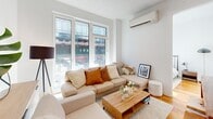 This 550 square foot apartment in Brooklyn offers a modern and efficient living space. The two-bedroom, one-bathroom layout maximizes functionality within its compact footprint. The open-concept living area is flooded with natural light from large windows, providing picturesque city views. The space features contemporary finishes throughout, including hardwood floors and crisp white walls.

The living room is thoughtfully arranged with a comfortable sectional sofa, wooden coffee table, and strategically placed lighting. The primary bedroom, measuring 110 square feet, boasts ample windows and is furnished with a stylish bed and minimal decor. The second bedroom, while compact, offers versatility as a guest room or home office.

The bathroom showcases a clean, modern design with neutral-toned tiles, a floating vanity, and a combination tub-shower. Throughout the apartment, built-in storage solutions help maximize the available space. The property is equipped with modern amenities, including wall-mounted air conditioning units for year-round comfort.

Located at 2715 Fulton St in Brooklyn, this apartment combines urban convenience with a cozy, well-designed living space, making efficient use of every square foot.