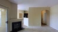 This single-floor residential space offers a comfortable and functional layout designed for everyday living. The living area serves as the heart of the home, highlighted by a classic black fireplace with a sleek surround that anchors the room as a focal point. Soft, neutral-toned carpet covers the floor, adding warmth and comfort underfoot, while the walls are finished in a warm beige tone that creates a calm and inviting atmosphere throughout.

The open layout connects the living area to the kitchen, which is partially visible and features dark cabinetry, providing a subtle contrast to the lighter tones of the surrounding space. A half-wall partition gracefully separates the kitchen area from the living room, maintaining a sense of openness while defining each zone.

An elegant arched doorway leads to additional areas of the home, adding an architectural detail that enhances the overall character of the space. Recessed lighting and standard overhead fixtures provide ample illumination throughout. The clean lines and neutral palette of this home create a versatile backdrop, ready to accommodate a variety of interior styles and furnishings. Overall, the space offers a balanced combination of architectural detail and practical design across its single level.