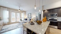 This thoughtfully designed single-floor residence seamlessly blends modern style with everyday comfort. The open-concept layout connects the kitchen and living area, creating a welcoming, airy atmosphere bathed in natural light. The kitchen is a standout, showcasing rich dark cabinetry reaching toward the ceiling, gleaming granite countertops, stainless steel appliances, a subway tile backsplash, and a central island with bar seating and elegant pendant lighting overhead — ideal for both casual dining and entertaining.

The living area extends naturally from the kitchen, featuring light hardwood-style flooring, a ceiling fan, and French doors that open to a private balcony with outdoor views. The space is bright and inviting, with generous windows dressed in sheer curtains and blinds.

The bedrooms offer a calm retreat, each equipped with a ceiling fan, large windows that invite natural light, and hardwood-style flooring. The primary bedroom includes access to a spacious walk-in closet with built-in shelving. Both bathrooms mirror the home's refined aesthetic, featuring dark cabinetry, granite vanity tops, large framed mirrors, tile flooring, and ample storage. In-unit laundry is also present, adding everyday convenience to this polished and functional residence.