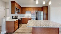 Located in Hickory, NC, this well-designed 2-bedroom, 2-bathroom single-story home offers a thoughtful layout with quality finishes throughout. The open-concept living and kitchen area is the heart of the home, highlighted by soaring vaulted ceilings, a ceiling fan, and a decorative chandelier. Large windows and a sliding glass door flood the space with natural light and provide outdoor views. The kitchen is well-appointed with rich warm-toned cabinetry, granite countertops, a central island, stainless steel appliances including a refrigerator, range, microwave, and dishwasher, and stylish pendant lighting. Wood-look luxury vinyl plank flooring runs throughout the main living areas, complementing the neutral color palette. The primary bedroom offers a comfortable footprint with plush carpeting, a bright window with blinds, and access to a spacious walk-in closet outfitted with wire shelving. The second bedroom also features soft carpeting and ample natural light. Both bathrooms are finished with granite-topped wood vanities and wood-look flooring; one includes a walk-in shower, while the other features a tub-shower combo. Two hallways and additional closets provide excellent storage throughout this clean, move-in-ready home.
