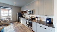 Located at 453 Snelling Ave N in Saint Paul, Minnesota, this modern studio unit offers a thoughtfully designed single-floor layout that maximizes both function and style. The open-concept living and sleeping area is anchored by warm hardwood-style flooring and neutral tones, creating a cohesive and inviting atmosphere. A sliding barn door adds a contemporary architectural touch while providing flexible space division between the sleeping and living zones. The living area benefits from large windows that flood the space with natural light and offer views of the surrounding neighborhood, complemented by a ceiling fan for year-round comfort. The fully equipped kitchen is a standout feature, showcasing flat-front cabinetry in a soft gray finish, open wood-accented shelving, a striking hexagonal tile backsplash, dark countertops, and a full suite of stainless steel appliances including a refrigerator, dishwasher, range, and microwave. The bathroom is finished with hardwood-style flooring, a tub-shower combination, and clean, minimalist fixtures with matte black hardware accents. Throughout the unit, recessed lighting and a carefully curated modern aesthetic make this a highly functional and visually appealing space in the heart of Saint Paul.