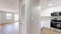 Located at 1008 Feagin Mill Rd in Warner Robins, Georgia, this two-story home offers five bedrooms and three bathrooms across two well-utilized floors. The ground floor houses the main living areas, including a combined kitchen and living room that flows openly between spaces. The kitchen features white shaker-style cabinetry, granite-look countertops, stainless steel appliances including a refrigerator, range, and over-the-range microwave, and a window providing natural light. The adjacent living room is generously sized with wood-look flooring, a ceiling fan, a textured ceiling, and a glass-panel door flanked by windows that allow ample natural light. A hallway and staircase connect to the upper floor, where additional bedrooms are situated. The bedrooms feature the same wood-look flooring, neutral gray walls, ceiling fans, and windows. Several bedrooms include built-in closets with louvered or panel doors. The bathrooms are finished with tile flooring, white vanities, and tub-shower combinations. Hallways on both floors provide efficient circulation throughout the home. The consistent neutral color palette and wood-look flooring create a cohesive aesthetic throughout.