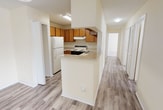 This single-story home offers a well-organized layout across three bedrooms and two bathrooms. The living area serves as the heart of the home, featuring notable vaulted ceilings that lend a sense of openness and volume to the space. A ceiling fan is installed overhead, and a window allows natural light to fill the room. The flooring throughout the main living areas and kitchen consists of durable wood-look laminate planks in a neutral gray-brown tone, providing a cohesive and easy-to-maintain surface.

A central hallway connects the living area to the rest of the home, with the kitchen positioned conveniently nearby. The kitchen is equipped with warm-toned wooden cabinetry, a range, refrigerator, dishwasher, and a sink, all arranged in an efficient layout with a pass-through opening to the adjacent living space.

The three bedrooms are carpeted in a neutral beige tone and each features windows that bring in natural light along with ceiling fans for added comfort. The two bathrooms are identically appointed, each featuring a tub-shower combination with white tile surround, wood-look flooring, and vanity storage. Textured ceilings are present throughout the home, contributing to its consistent aesthetic.