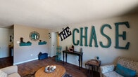 This single-floor home is defined by a lively, personalized aesthetic that carries throughout each room. The living area serves as the centerpiece of the space, featuring rich hardwood-style flooring, a textured ceiling, and a striking wall display of large teal letters spelling out "THE CHASE," giving the room a bold, character-filled identity. A sliding glass door at the far end of the living room floods the space with natural light while offering a view of the outdoor greenery beyond.

The kitchen is efficiently laid out with dark cabinetry, black appliances including a gas range and full-size refrigerator, and light countertops. Adjacent to the kitchen, the dining area provides an intimate setting accented by a ceiling fan, a reclaimed wood wall panel, and warm decorative touches.

The primary bedroom showcases a vibrant teal accent wall paired with mirrored wall panels, plush carpeting, and a sophisticated silver dresser, creating an elegant and restful retreat. A secondary bedroom carries a sporty theme, complete with carpeted floors, a rustic wood dresser with mirror, and motivational wall signage.

The bathroom features a full tub-shower combination with a curtain rod, a toilet, and vanity, finished with colorful, coordinated accents. Throughout the home, cohesive teal and warm-tone décor ties each space together into a cheerful and well-curated interior.