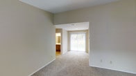 This two-floor residence is designed with a clean, functional layout and a neutral color palette that creates a bright, welcoming atmosphere throughout. The interior walls are finished in a warm beige tone, complementing the plush wall-to-wall carpeting that runs through the living areas, adding comfort underfoot.

A standout feature of the main living area is the full-width sliding glass door, which floods the space with natural light and provides direct views of the surrounding greenery outdoors. The open sightlines between rooms contribute to a spacious, airy feel. Ceiling-mounted HVAC vents are discreetly integrated into the design, ensuring efficient climate control throughout.

Adjacent to the living area, a hallway leads to a bathroom, which is visible from the main space. The bathroom features warm wood-toned cabinetry and a vanity with overhead lighting, offering a functional and practical layout.

The overall design of the space prioritizes simplicity and livability, with neutral finishes that provide a versatile backdrop adaptable to a variety of interior styles. The two-floor layout offers additional living or sleeping areas beyond what is visible, expanding the overall functionality of the residence.