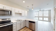 Located at 651 Meeting St in Charleston's vibrant 29403 zip code, this single-floor residence offers a thoughtfully designed layout with modern finishes throughout. The kitchen serves as a functional centerpiece, featuring white shaker-style upper cabinets, gray lower cabinetry, and a classic white subway tile backsplash. Light quartz countertops provide ample workspace, while a full suite of stainless steel appliances — including a refrigerator, electric range, over-the-range microwave, and dishwasher — completes the space. Pendant lighting adds a refined touch above the peninsula, which opens directly toward the living area. The living space benefits from a large bank of windows that flood the room with natural light and offer views of the surrounding neighborhood. A ceiling fan contributes to year-round comfort, while neutral-toned carpet underfoot adds warmth. The bathroom is well-sized, finished with wood-look luxury vinyl plank flooring, a vanity with gray cabinetry, and a bathtub/shower combination. An adjacent walk-in closet provides generous storage. Throughout the unit, light-toned walls and consistent flooring create a clean, cohesive aesthetic suited to contemporary living in the heart of Charleston.