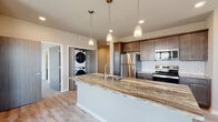 This single-floor residence showcases a thoughtfully designed layout with modern finishes throughout. The kitchen serves as a central highlight, featuring rich dark-stained shaker cabinetry, granite countertops with striking natural veining, a full suite of stainless steel appliances, and a classic white subway tile backsplash. A large kitchen island with an integrated sink and pendant lighting overhead adds both functionality and style. Light-toned hardwood-style flooring runs throughout the main living and kitchen areas, creating a cohesive, bright aesthetic. A stacked washer and dryer unit is conveniently integrated near the kitchen.

The bedrooms are carpeted and well-lit by large windows that allow ample natural light. The primary bedroom includes a ceiling fan and generous proportions, while a spacious walk-in closet with wire shelving and dedicated hanging space provides substantial storage. An additional closet near the hallway features wood-tone paneling and built-in shelving.

The bathrooms are finished with the same granite countertops found in the kitchen, undermount sinks, modern chrome fixtures, and large mirrors. Neutral gray walls and light flooring maintain a clean, contemporary feel throughout the entire residence.