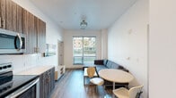 This single-floor unit is designed with a clean, modern aesthetic, incorporating consistent wood-look flooring, white walls, and contemporary fixtures throughout. The open-concept living and dining area serves as the heart of the unit, where a sectional sofa anchors the lounge space beside a large window fitted with horizontal blinds, allowing natural light and outdoor views of surrounding greenery. A round dining table with wooden chairs completes the shared living space, creating a functional and welcoming environment.

The kitchen runs along one wall in a galley-style configuration, featuring dark wood-grain cabinetry, white quartz countertops, a geometric tile backsplash, and a full suite of stainless steel appliances including a range, microwave, dishwasher, and refrigerator. Recessed lighting illuminates the kitchen and entry corridor, which leads directly to the front door.

The bedrooms are well-proportioned and simply appointed, each with wood-look flooring, white walls, and built-in storage options such as wardrobes. One bedroom includes a window with outdoor views, while another connects directly to a private bathroom. The bathrooms feature wood-toned vanities, white countertops, large mirrors, and shower-tub combinations, maintaining the unit's cohesive, neutral palette throughout.