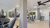 Located at 3701 Southwest 34th Street in Gainesville, Florida, this fitness center is a thoughtfully designed exercise facility that offers a comprehensive workout environment within a single, open floor. The space features light wood-tone flooring in the primary workout zone, transitioning to a polished tile surface near the entrance, and is kept bright and airy through a generous bank of floor-to-ceiling windows along one wall that invite abundant natural light and outdoor views.

The cardio section is equipped with multiple treadmills, elliptical trainers, and stationary bikes positioned to take advantage of the natural light and window views. A full-length mirrored wall amplifies the sense of openness while allowing users to monitor their form. Overhead, sleek ceiling fans maintain comfortable air circulation throughout the space.

The strength training area is well-appointed with a variety of cable and weight machines, adjustable benches, a dumbbell rack, and a dedicated functional fitness station stocked with medicine balls, resistance bands, and exercise balls on wall-mounted storage racks. Structural columns are integrated cleanly into the design, finished in a neutral gray tone that complements the modern aesthetic.

Decorative touches, including botanical moss wall art and colorful framed prints, add a polished, welcoming ambiance. A teal built-in storage credenza near the entrance provides a practical organizational element. The facility is finished with recessed lighting throughout, ensuring consistent illumination across all workout zones.