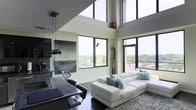 Located at 240 S Harrison Street in East Orange, New Jersey, this impressive two-floor residence showcases a bold, contemporary design that immediately draws the eye upward with its dramatic double-height ceilings. The open-concept living and kitchen area serves as the heart of the home, bathed in abundant natural light streaming through expansive floor-to-ceiling windows that frame sweeping panoramic views of the surrounding cityscape and skyline. The living space is anchored by rich dark hardwood flooring, which provides a striking contrast against the bright, white walls and high ceilings. A sleek, modern kitchen features dark granite countertops, a breakfast bar with seating, and pendant lighting, seamlessly integrating with the living area for an effortless flow. Large windows wrap around multiple sides of the space, ensuring that natural light and city views are ever-present throughout the day. The elevated position of the residence amplifies the sense of openness, making the interior feel exceptionally spacious and airy. The two-floor layout offers distinct living zones, balancing open entertaining areas with more private spaces above. Overall, the residence exudes a sophisticated, urban ambiance defined by high-end finishes, architectural drama, and a strong connection to its vibrant East Orange surroundings.