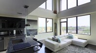 Located at 240 S Harrison Street in East Orange, New Jersey, this impressive two-floor residence showcases a bold, contemporary design that immediately draws the eye upward with its dramatic double-height ceilings. The open-concept living and kitchen area serves as the heart of the home, bathed in abundant natural light streaming through expansive floor-to-ceiling windows that frame sweeping panoramic views of the surrounding cityscape and skyline. The living space is anchored by rich dark hardwood flooring, which provides a striking contrast against the bright, white walls and high ceilings. A sleek, modern kitchen features dark granite countertops, a breakfast bar with seating, and pendant lighting, seamlessly integrating with the living area for an effortless flow. Large windows wrap around multiple sides of the space, ensuring that natural light and city views are ever-present throughout the day. The elevated position of the residence amplifies the sense of openness, making the interior feel exceptionally spacious and airy. The two-floor layout offers distinct living zones, balancing open entertaining areas with more private spaces above. Overall, the residence exudes a sophisticated, urban ambiance defined by high-end finishes, architectural drama, and a strong connection to its vibrant East Orange surroundings.