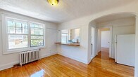 Located in Toronto's lively Queen Street East neighbourhood, this one-bedroom, one-bathroom unit offers a well-organized, efficient layout across a single floor. Warm-toned hardwood floors run throughout the space, lending a classic character that complements the clean white walls and bright, airy feel.

The living room is a welcoming area filled with natural light from large windows that frame neighbourhood views. A classic cast-iron radiator provides reliable heating, while a textured ceiling adds a touch of vintage charm. An elegant arched passageway connects the living area to the kitchen, which features a pass-through counter and open shelving, maximizing the sense of openness.

The bedroom is a comfortable, well-proportioned room with its own large window and radiator, ensuring both light and warmth. Smooth white walls and gleaming hardwood floors create a calm, restful atmosphere.

The bathroom is thoughtfully appointed with neutral tile work surrounding a full soaker tub and shower combination. A window provides natural light and ventilation, while a white vanity with a vessel sink and wood-toned countertop adds a modern touch to the otherwise classic design.

Two hallways connect the rooms efficiently, contributing to a logical and practical flow throughout the unit. Overall, this space combines timeless architectural details with functional living in one of Toronto's most sought-after neighbourhoods.