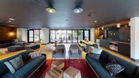 Located in the heart of San Diego's vibrant Bankers Hill/Downtown neighborhood, this single-floor communal space at 372 Fourth Ave offers a thoughtfully designed environment that blends comfort, functionality, and contemporary style. The open-plan layout seamlessly connects multiple distinct zones, creating a fluid and inviting atmosphere throughout.

The main lounge area is anchored by a striking fireplace set against a bold geometric patterned tile wall, complemented by plush dark sofas, accent chairs with Southwestern-inspired cushions, and layered area rugs over warm cork flooring. Pendant and dome-style ceiling lights add a mid-century modern character to the space. A dedicated lounge nook features built-in shelving and additional seating, perfect for relaxed gatherings.

The kitchenette is a design highlight, boasting floor-to-ceiling dark glossy tile backsplash, warm wood-paneled walls and ceiling, sleek grey countertops, and modern cabinetry with bold gold and black accents. A separate dining area with a long communal table provides ample space for shared meals or collaborative work.

A private meeting room features a round wood table, leather chairs, an industrial-style pendant light, and a stunning textured penny-tile accent wall. Large sliding glass doors open to an outdoor terrace, flooding the interior with natural light and extending the usable space outdoors.