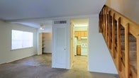 Located at 1 Bosquet Court in Summerville, South Carolina, this two-story home offers a practical and comfortable layout designed for everyday living. The main level features a carpeted living area that provides a warm, inviting atmosphere, complemented by a ceiling fan that aids in air circulation. Built-in shelving along one wall offers convenient storage and display space, adding a functional architectural touch to the room. A louvered closet door provides additional storage just off the main living area, while an HVAC vent overhead ensures year-round climate comfort. The staircase, featuring a classic wooden railing, connects the main level to the upper floor, adding a traditional design element to the interior. The kitchen is accessible directly from the living area and is equipped with wooden cabinetry, a white range, and tile flooring, offering a clean and efficient workspace. Natural light filters into the living space through a window, brightening the room and creating an open feel. The overall layout of this home is well-organized, with clearly defined spaces that transition smoothly from one to the next, making it a straightforward and livable property in the heart of Summerville, SC.