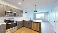 This thoughtfully designed 1-bedroom, 1-bathroom unit offers a clean, modern aesthetic across a single floor. The open-concept kitchen and living area serves as the heart of the space, featuring gray shaker-style cabinetry, crisp white subway tile backsplash, white quartz countertops, and a full suite of stainless steel appliances including an electric range with over-the-range microwave and dishwasher. Stylish black pendant lights hang above the kitchen, complementing the matte black hardware throughout. Light-toned hardwood-style flooring runs continuously through every room, enhancing the sense of openness and cohesion. The living area receives generous natural light through a large window with outdoor views. The bedroom is a comfortable, well-proportioned room equipped with a ceiling fan and a window that allows in natural light. Two closets provide ample storage, including a walk-in closet with wire shelving systems. The bathroom features a full tub-shower combination wrapped in classic white subway tile and accented with matte black fixtures. A dedicated in-unit laundry closet with a stacked washer and dryer adds everyday convenience. Neutral wall tones and clean lines throughout create a fresh, move-in-ready atmosphere.