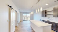 This contemporary single-floor unit showcases a clean, modern design highlighted by light hardwood flooring and crisp white walls throughout. The open-concept layout seamlessly connects the kitchen, dining, and living areas, creating a bright and airy atmosphere filled with natural light.

The chef's kitchen is a standout feature, outfitted with rich dark wood cabinetry, white quartz countertops, and a classic subway tile backsplash. A generously sized center island with pendant lighting provides both additional prep space and a natural gathering point. Stainless steel appliances, including a French door refrigerator, electric range, built-in microwave, and dishwasher, complete the well-appointed kitchen.

The living area flows directly to a private balcony through a full-width sliding glass door, offering outdoor views and an abundance of natural light. A stylish sliding barn door adds a contemporary architectural detail to the main living space.

The bedrooms are well-proportioned, each featuring hardwood flooring and generous windows that bring in natural light. One bedroom includes direct balcony access via its own sliding glass door. The bathroom is finished with tile flooring, a white quartz vanity, and a tub-shower combination, maintaining the unit's consistent modern aesthetic throughout.