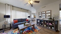 Located at 1300 W Warner Rd in Gilbert, Arizona, this single-floor residence offers a thoughtfully designed layout with stylish finishes throughout. The living room is a welcoming focal point, bathed in natural light from large windows dressed with horizontal blinds and elegant grommet curtains. Vaulted ceilings and a ceiling fan add to the airy feel, while wood-look flooring runs seamlessly through the main living areas. An adjacent dining area provides a bright, dedicated space for meals, complemented by a sliding glass door that invites additional natural light. The kitchen features gray cabinetry, granite-style countertops, and a full suite of black appliances including a range, over-the-range microwave, dishwasher, and refrigerator, all set over durable wood-look flooring. The primary bedroom is generously sized with plush carpet, a sliding glass door with outdoor views, and a ceiling fan overhead. The primary bathroom includes gray vanity cabinetry, granite-style countertops, and wood-look flooring, with access to a walk-in closet area. A dedicated laundry space houses a full-size, side-by-side washer and dryer. The overall ambiance is warm and livable, with consistent finishes tying the home together cohesively.