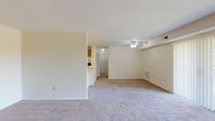 This single-floor residence offers a thoughtfully arranged layout that balances open communal space with functional private areas. The living room is generously sized, finished with plush neutral carpeting and a ceiling fan overhead. A half-wall partition separates it from the kitchen, creating an open, connected feel while maintaining defined zones. Pendant lighting above the kitchen counter adds a warm accent to the space.

The kitchen is well-appointed with warm oak cabinetry offering abundant upper and lower storage, light-toned countertops, and white appliances including a gas range, dishwasher, and refrigerator. Light tile flooring completes the practical, easy-to-maintain cooking space.

The bedrooms feature wood-look laminate flooring and neutral walls, with windows that invite natural light. One bedroom includes access to a spacious walk-in closet lined with multiple shelving tiers and hanging rods on both sides, providing excellent storage capacity.

The bathroom includes a full-size tub and shower combination with clean white surroundings and tile flooring. Throughout the unit, the consistent neutral color palette and updated finishes create a cohesive, move-in-ready environment.