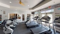 Located at 2426 Channel Marker Way in Hanahan, South Carolina, this well-equipped fitness center offers a comprehensive workout environment designed to meet a variety of exercise needs. The single-floor facility is thoughtfully organized into distinct workout zones, each catering to different training styles.

The cardio area is lined with multiple treadmills and a stair climber, positioned along large windows that allow abundant natural light to fill the space. A mounted flat-screen TV provides entertainment during workouts, while motivational typography — featuring words like "goals," "fitness," "ambition," and "lifestyle" — adorns the walls, creating an energizing atmosphere.

The strength training section features a well-stocked dumbbell rack with a wide range of free weights, a large wall-mounted mirror that visually expands the room, and a standing punching bag for functional fitness training. Dark rubber flooring throughout provides traction and durability underfoot.

A separate cycling zone houses multiple spin bikes and upright stationary bikes, elegantly divided from the rest of the space by a decorative chain curtain partition. Recessed lighting and high ceilings contribute to the open, airy feel of the room. A water station and informational postings are conveniently accessible near the cycling area. Overall, the space strikes a balance between functionality and a motivating, modern aesthetic.