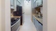 This single-story residence offers a thoughtfully designed layout with a neutral gray color palette and light wood-style flooring that flows consistently throughout the space. The galley-style kitchen is a standout feature, equipped with gray shaker cabinetry, granite countertops, a textured stone tile backsplash in warm earth tones, a stainless steel refrigerator and range, and a double-basin sink with a matte black faucet. A ceiling fan with an overhead pendant light adds both function and character to the kitchen area. A pass-through window with a granite ledge connects the kitchen to the adjacent living and dining areas, enhancing the open feel of the space. The living area is generously proportioned, featuring vaulted ceilings, soft gray walls, and a sliding glass door fitted with vertical blinds that allows natural light to filter in. A separate bedroom offers a window with an outdoor view, a textured ceiling, and a built-in closet with sliding panel doors. The bathroom includes a soaking tub with white subway tile surround and matte black hardware accents. Ample closet storage and a clean, modern finish complete this well-appointed space.