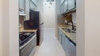This single-story residence offers a thoughtfully designed layout with a neutral gray color palette and light wood-style flooring that flows consistently throughout the space. The galley-style kitchen is a standout feature, equipped with gray shaker cabinetry, granite countertops, a textured stone tile backsplash in warm earth tones, a stainless steel refrigerator and range, and a double-basin sink with a matte black faucet. A ceiling fan with an overhead pendant light adds both function and character to the kitchen area. A pass-through window with a granite ledge connects the kitchen to the adjacent living and dining areas, enhancing the open feel of the space. The living area is generously proportioned, featuring vaulted ceilings, soft gray walls, and a sliding glass door fitted with vertical blinds that allows natural light to filter in. A separate bedroom offers a window with an outdoor view, a textured ceiling, and a built-in closet with sliding panel doors. The bathroom includes a soaking tub with white subway tile surround and matte black hardware accents. Ample closet storage and a clean, modern finish complete this well-appointed space.