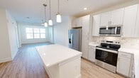 Located at 200 Brooklawn St in Farragut, TN, this well-appointed 2-bedroom, 2-bathroom single-floor residence offers a thoughtfully designed layout with modern finishes throughout. The open-concept kitchen serves as the heart of the home, showcasing white shaker-style cabinetry extending to the ceiling, a large center island with a crisp white countertop, a marble-look tile backsplash, and a full suite of stainless steel appliances including a French door refrigerator, electric range, and built-in microwave. Stylish pendant lights hang above the island, complementing the light hardwood-style flooring that flows through the main living areas. The living room receives ample natural light through large windows fitted with horizontal blinds. Both bedrooms are carpeted and feature ceiling fans, neutral walls, and windows with outdoor views. The primary bedroom is generously sized and connects conveniently to a well-finished bathroom. The bathrooms are outfitted with white subway tile tub surrounds, white vanities, and light wood flooring. A dedicated laundry area houses a full-size top-load washer and dryer. Additional storage is provided by two closets, and a hallway connects the rooms with clean, white-walled finishes throughout.