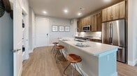 This single-floor residence offers a thoughtfully designed open-concept layout that seamlessly connects the kitchen, dining, and living areas. The kitchen is a standout feature, equipped with stainless steel appliances, warm wood-toned cabinetry, a subway tile backsplash, and a generous quartz island with bar seating — ideal for both meal prep and casual dining. Recessed lighting illuminates the space, which flows directly into the living area highlighted by durable wood-look flooring, a ceiling fan, a wall-mounted television, and a glass door providing access to an outdoor balcony with exterior views.

A secondary sitting or living nook offers additional comfort, featuring large windows with horizontal blinds that invite ample natural light, complemented by soft neutral wall tones. The bedrooms are carpeted and well-proportioned, each accommodating a king-sized bed with room to spare. One bedroom enjoys a large window with outdoor views, while the other is appointed with tasteful wall décor.

The bathroom presents a refined finish with a wood-framed vanity mirror, quartz countertops, wood-grain cabinetry, and large-format tile flooring. A walk-in closet with built-in shelving and hanging rods provides generous storage. Throughout the residence, a cohesive neutral palette and modern finishes create a clean, contemporary ambiance.