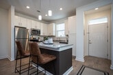 Located at 1000 Infinity Dr in Maryville, Tennessee, this single-story residence offers a thoughtfully designed open-concept floor plan with modern finishes throughout. Light wood-style flooring flows seamlessly across the entire unit, creating a cohesive and airy feel.

The kitchen serves as a central hub of the home, featuring crisp white cabinetry, granite countertops, stainless steel appliances, a double-basin sink beneath a natural light window, and a large center island with pendant lighting overhead. The kitchen opens directly into a dining area and a comfortable living room, which is equipped with a ceiling fan and receives ample natural light.

The two bedrooms are generously proportioned, each outfitted with ceiling fans and large windows that invite natural light and exterior views. Both rooms offer walk-in closet space with built-in shelving for organized storage.

The bathroom is well-appointed with white cabinetry, granite countertops, a wide vanity mirror with overhead lighting, and direct access to a dedicated walk-in closet. Additional storage is provided by a mirrored walk-in closet featuring wire shelving and hardwood-style flooring. The overall ambiance is bright, clean, and modern, making this a highly functional and welcoming living space in Maryville, TN.