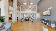 Located at 15024 North 90th Street in Scottsdale, Arizona, this expansive community clubhouse at Overture North Scottsdale spans an impressive footprint across a single floor, offering a sophisticated and welcoming environment for residents and guests alike.

The heart of the space is a dramatic grand lounge featuring soaring double-height ceilings, a mezzanine level with glass railings, and a striking linear fireplace framed in stone tile. Large arched windows and floor-to-ceiling glass panels flood the area with natural light, while warm travertine-style tile flooring anchors the open layout. Comfortable seating arrangements with upholstered sofas and accent chairs create inviting conversation areas throughout.

Adjacent to the lounge is a sleek, well-appointed kitchen featuring a generous marble-topped island with bar seating, warm wood cabinetry, stainless steel appliances, and globe pendant lighting. A vibrant botanical-patterned backsplash adds a touch of personality to the refined design.

The dining area accommodates multiple tables beneath elegant drum pendant lights, with direct access to an outdoor patio space. A dedicated reception area includes a built-in desk, patterned wallcovering, and a welcoming chalkboard sign. Large-panel windows throughout ensure views of the surrounding Scottsdale landscape. The space is completed by a fitness center, accessible through wide double doors.