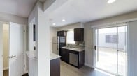 This single-floor residence offers a thoughtfully designed layout that balances functionality with modern style. The kitchen serves as a central highlight, showcasing dark espresso cabinetry paired with light granite countertops for a striking contrast. A mosaic tile backsplash adds texture and visual interest, while recessed lighting illuminates the space from above beneath a textured ceiling. Stainless steel appliances, including a refrigerator and dishwasher, lend a contemporary, cohesive look throughout the kitchen. A window above the sink allows natural light to filter in, enhancing the bright and airy feel of the space. Adjacent to the kitchen, a sliding glass door opens to an outdoor patio area, seamlessly connecting indoor and outdoor living. The flooring throughout features wood-look planks that add warmth and durability underfoot. A partial wall with a light granite countertop edge hints at an open-concept connection to the living area, promoting a sense of flow and spaciousness throughout the home. The overall ambiance is clean, modern, and move-in ready.