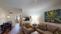 This single-floor residence offers a thoughtfully arranged layout that maximizes comfort and functionality. The living area serves as the heart of the home, featuring warm neutral tones, plush seating, and a textured popcorn ceiling. A built-in wall niche provides a dedicated spot for a television, while bold botanical artwork adds a vibrant focal point to the room. Wood-look flooring flows through the main living spaces, lending warmth and continuity, while a front entry door flanked by windows with white shutters allows natural light to filter in.

The galley-style kitchen is efficiently designed with rich wood cabinetry lining both walls, light countertops, and black appliances including a range and refrigerator. A single-basin sink and dishwasher complete the functional workspace, with wood-look flooring carrying through from the main living area.

The bedroom is a tranquil retreat with soft carpet underfoot, a ceiling fan for year-round comfort, and a window with shutters that allows natural light to brighten the space. An adjacent bathroom features a vanity with a single-basin sink, light countertop, and mirrored cabinetry, finished with wood-look flooring. Overall, the space presents a warm, livable environment with consistent finishes throughout.