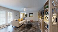 This single-floor residence is thoughtfully laid out across a comfortable footprint, featuring two bedrooms, a spacious living area, a dedicated dining space, a full kitchen, and at least one full bathroom. The living room serves as the central gathering space, finished with wood-style plank flooring, a textured ceiling, and ceiling fan lighting. A sliding glass door invites natural light and connects the space to the outdoors, while a seating area with bold navy accent chairs adds a stylish touch. The dining area features light wood flooring, a bold yellow accent wall, and large windows that brighten the space, complemented by round wall mirrors and floating shelves. The kitchen is outfitted with white shaker cabinetry, light stone-look countertops, and stainless steel appliances including a range, microwave, and dishwasher. The primary bedroom features plush carpet, a bold navy accent wall, and a ceiling fan, while the secondary bedroom offers a sage green accent wall and natural window light. The bathroom includes white tile flooring, a single vanity with ample storage, and a tub-shower combination. Throughout, the space maintains a cohesive, modern aesthetic with vibrant accent colors and tasteful décor.
