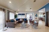 Located in Houston's Briar Forest neighborhood, this single-level community amenity space offers a thoughtfully designed interior that balances comfort and functionality. The main lounge area makes an immediate impression with its distinctive vaulted shiplap ceiling, large windows dressed with sheer curtains, and light-toned tile flooring throughout. Plush sectional seating in rich brown tones, accented by vibrant teal throw pillows, is arranged around a glass coffee table atop a bold patterned area rug, creating an inviting gathering space. A sleek arc floor lamp provides ambient lighting, complemented by recessed ceiling fixtures. Adjacent to the lounge, a cozy dining nook features a glass-top table with acrylic chairs set against a bold blue accent wall, with direct sightlines into the fitness center beyond a full-height glass partition wall — keeping the space feeling open and connected. The fitness center is well-lit with natural light and equipped with a variety of exercise machines and free weights. The kitchen is outfitted with rich dark wood cabinetry, granite countertops, mosaic tile backsplash, stainless steel appliances, and a generous island beneath elegant globe pendant lights. A window above the sink brings in natural light. Decorative framed mirrors in the hallway add depth and visual interest throughout the space.