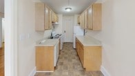 This single-floor residence presents a clean, functional layout spread across several interconnected rooms. Warm-toned hardwood flooring flows throughout the living and sleeping areas, lending a classic character to the interior. The main living area is generously sized, featuring a large multi-pane window that invites natural light and a traditional cast-iron radiator beneath it, indicative of classic building construction. Neutral cream-toned walls throughout keep the space feeling bright and open.

The galley-style kitchen is efficiently arranged with light wood cabinetry lining both walls, offering ample upper and lower storage. Light-toned countertops, a white electric range, and a white refrigerator provide all essential appliances. A tile-patterned floor grounds the space practically.

Additional rooms, visible from both the floor plan and individual images, include well-proportioned spaces with the same warm hardwood flooring and neutral walls, suitable for use as bedrooms or flexible living areas. Each room connects through interior doorways, creating a cohesive flow. The overall ambiance is straightforward and classic, with traditional architectural details and a clean, move-in-ready presentation.