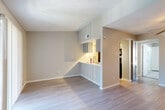 This efficiently designed 1-bedroom, 1-bathroom residence offers a thoughtful layout across a single floor, making excellent use of its compact footprint. The living area is a standout space, featuring vaulted ceilings, light wood-style flooring, neutral warm-toned walls, and a classic fireplace with a clean surround — an inviting focal point for the room. Natural light enters through a windowed entry door and a sliding glass door fitted with vertical blinds, suggesting access to an outdoor area. A pass-through opening connects the living room to the galley-style kitchen, which is outfitted with grey shaker cabinetry, white countertops, a stainless steel sink with a modern faucet, and black appliances including a refrigerator, range, and dishwasher. Track lighting overhead adds a practical touch. The bedroom offers plush carpeting, a ceiling fan, a window with blinds bringing in natural light, and access to a dedicated closet area that also houses in-unit washer and dryer connections. The bathroom is clean and functional, featuring a full tub-shower combination with white tile surround and wood-look flooring. Textured ceilings are consistent throughout, adding subtle architectural character to the overall space.