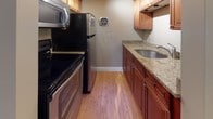 Located at 78 Manor in Manchester, New Hampshire, this single-floor residence offers a clean, functional layout designed for comfortable everyday living. The open living area is a standout feature, showcasing warm hardwood flooring, neutral-toned walls, and bright natural light streaming through well-positioned windows. Baseboard heating is present throughout, ensuring year-round comfort. The spacious living room provides an open, airy feel with ample room to arrange furnishings, while a dedicated bedroom offers a quiet retreat with its own window overlooking a wooded outdoor setting and a wall-mounted air conditioning unit for additional climate control. The galley-style kitchen is thoughtfully appointed with rich wood cabinetry, granite countertops, a stainless steel sink, and a full suite of stainless steel appliances including a range, refrigerator, and microwave. The full bathroom features white tile walls, a tub and shower combination with a safety grab bar, tile flooring, and a window that allows for natural ventilation. Clean white trim and baseboards throughout the unit contribute to a polished, cohesive aesthetic. This well-maintained residence combines practical design with updated finishes in a convenient Manchester location.