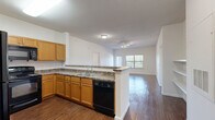 Located at 4647 Wenda St in Houston, TX, this single-story, 2-bedroom, 2-bathroom home offers a well-organized layout with consistent wood-style flooring running throughout every room. The open-concept kitchen and living area serves as the heart of the home, where a peninsula-style counter with granite-look surfaces separates the kitchen from the living space. The kitchen is equipped with warm honey-toned cabinetry, ample upper and lower storage, granite-style countertops, and black appliances including a refrigerator, range, and over-the-range microwave. The living room receives natural light through large windows fitted with horizontal blinds. Both bedrooms are generously proportioned, each featuring a ceiling fan with light fixture, windows with outdoor views, and access to dedicated closet space. The primary bedroom includes a spacious walk-in closet outfitted with built-in shelving and hanging rods. Both bathrooms are similarly appointed with wood-tone vanity cabinetry, white countertops, a tub/shower combination with a curtain rod, and consistent wood-style flooring. The neutral color palette of soft white walls and warm flooring tones creates a cohesive and functional living environment throughout the home.