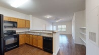 Located at 4647 Wenda St in Houston, TX, this single-story, 2-bedroom, 2-bathroom home offers a well-organized layout with consistent wood-style flooring running throughout every room. The open-concept kitchen and living area serves as the heart of the home, where a peninsula-style counter with granite-look surfaces separates the kitchen from the living space. The kitchen is equipped with warm honey-toned cabinetry, ample upper and lower storage, granite-style countertops, and black appliances including a refrigerator, range, and over-the-range microwave. The living room receives natural light through large windows fitted with horizontal blinds. Both bedrooms are generously proportioned, each featuring a ceiling fan with light fixture, windows with outdoor views, and access to dedicated closet space. The primary bedroom includes a spacious walk-in closet outfitted with built-in shelving and hanging rods. Both bathrooms are similarly appointed with wood-tone vanity cabinetry, white countertops, a tub/shower combination with a curtain rod, and consistent wood-style flooring. The neutral color palette of soft white walls and warm flooring tones creates a cohesive and functional living environment throughout the home.