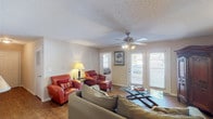 This single-floor residence offers a thoughtfully arranged layout encompassing a living room, dining area, kitchen, two bedrooms, and a full bathroom. The living room serves as the central gathering space, featuring wood-look flooring, a textured ceiling, and a ceiling fan with integrated lighting. French doors flood the room with natural light and provide direct access to an outdoor deck, while a decorative armoire adds a classic touch alongside framed wall art. Two leather accent chairs and a glass-top coffee table complete the seating arrangement.

The galley-style kitchen features white cabinetry, light countertops, a stainless steel sink, and white appliances, flowing directly into the adjacent dining area. The dining space is anchored by a round glass-top table beneath a pendant light, with an arched opening connecting the two areas seamlessly.

The primary bedroom is carpeted and accommodates a full-sized bed, while the second bedroom features twin beds positioned on either side of a shared nightstand beneath a window. The bathroom is well-equipped with white cabinetry, a large vanity mirror with overhead lighting, wood-look flooring, and a shower-tub combination.