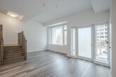 Located at 55 Quebec Ave in Toronto's vibrant Junction neighbourhood, this two-storey unit offers 2 bedrooms and 3 bathrooms across two well-proportioned floors. The main level features an open-concept layout combining the living, dining, and kitchen areas, all finished with light hardwood-style flooring. The contemporary kitchen is equipped with stainless steel appliances, two-tone cabinetry, a patterned tile backsplash, and a freestanding island with built-in shelving, topped with a white quartz-style surface and accented by a modern pendant light. Large windows and a glass-panel door on the main floor flood the space with natural light and provide direct access to the balcony, offering outdoor views of surrounding greenery and the neighbourhood streetscape. A wood-railed staircase connects both floors. The upper level houses the two bedrooms, including a generously sized primary bedroom, alongside the remaining bathrooms. The bathrooms are finished in a clean, modern style — one featuring a double-sink vanity with light wood cabinetry and large mirrors, and another with a soaker tub surrounded by floor-to-ceiling neutral stone-look tile. Throughout, the unit maintains a bright, minimalist aesthetic with white walls and contemporary finishes.