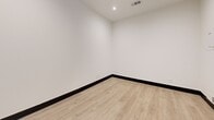 Located at 301 Nichols St in Fort Worth, Texas, this single-room space offers a clean, modern interior designed for efficient use. The room features light-toned hardwood-style flooring that contrasts neatly with bold dark baseboards, lending a contemporary edge to the otherwise minimalist design. Bright white walls and recessed ceiling lighting create a well-lit, open atmosphere throughout the space.

A glass-paneled entry door fitted with horizontal blinds allows natural light to filter into the room while maintaining privacy. A small horizontal clerestory window above the door further supplements the natural lighting. The ceiling hosts a central HVAC vent for climate control, and an additional floor-level vent ensures consistent airflow throughout.

One wall features a mounted utility panel, and multiple electrical outlets are conveniently distributed around the room, making the space highly functional. The overall layout is straightforward and open, providing flexibility for a variety of uses. The clean finishes, neutral color palette, and practical amenities combine to create a tidy, functional environment suited for professional or personal use.