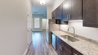 Located at 380 Mather St in Hamden, Connecticut, this thoughtfully designed single-floor unit makes efficient use of its compact footprint. Warm-toned hardwood-style flooring flows throughout, tying together the space with a cohesive, contemporary aesthetic.

The kitchen is a standout feature, outfitted with rich dark espresso cabinetry, granite countertops, and a full suite of stainless steel appliances including a gas range, over-the-range microwave, dishwasher, and refrigerator. Under-cabinet lighting adds a refined touch, while a stainless steel sink completes the functional layout.

The main living area is open and airy, bathed in natural light from a window at the end of the hallway. Neutral-toned walls provide a clean backdrop, and the open arched entry to the closet adds architectural interest while offering generous built-in storage with shelving.

The bathroom is well-appointed, featuring a full tub-shower combination, a dark wood vanity with a white countertop and undermount sink, a framed mirror, and polished chrome fixtures—all set against light neutral walls that create a bright, clean atmosphere.

Two hallways connect the spaces seamlessly, enhancing the sense of flow throughout the unit. This move-in-ready home combines modern finishes with practical design in a desirable Hamden location.