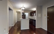 Located at 755 W Big Beaver Rd in Troy, Michigan, this single-floor unit offers a well-appointed interior with a thoughtful mix of finishes and functional design throughout. The open living area is a standout feature, showcasing rich, dark hardwood flooring that extends across the main living spaces, complemented by neutral-toned walls and a textured ceiling. A sliding glass door floods the room with natural light and provides access to an outdoor area, while a wall-mounted air conditioning unit and baseboard heating ensure year-round comfort. An entry closet with open shelving offers convenient storage just inside the front door. The kitchen is efficiently designed with dark espresso cabinetry, granite countertops, a subway tile backsplash, stainless steel appliances including a refrigerator and range, and a pass-through counter that connects to the main living space. A dedicated pantry with built-in shelving adds generous storage capacity. The bedroom features plush carpeting, a large sliding glass window with outdoor views, and baseboard heating. The bathroom is finished with floor-to-ceiling large-format dark gray tile surrounding a soaking tub and shower combination, paired with polished chrome fixtures for a clean, modern aesthetic.
