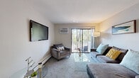 Located at 915 W Panorama Dr in Palatine, IL, this single-floor residence offers a well-designed layout with a cohesive, contemporary aesthetic. The living room is carpeted and inviting, centered around a wall-mounted television and a sliding glass door that opens to a private balcony with tree-lined views, allowing natural light to fill the space. A baseboard heating system and wall-mounted air conditioning unit ensure year-round comfort.

The kitchen is a functional highlight, featuring rich dark-stained cabinetry, light quartz countertops, and a full suite of stainless steel appliances, including a range, microwave, dishwasher, and refrigerator. Light wood-look flooring adds warmth and continuity to the kitchen and dining area.

The dining space accommodates a round table with ceiling fan overhead, creating a relaxed setting for meals. A secondary room with carpeting and a window provides flexible living options. The bedroom is generously proportioned with soft carpeting and a calm, neutral palette. The bathroom features a tub-shower combination with tile surround, a wood-toned vanity, and light flooring, delivering a clean, modern finish throughout.