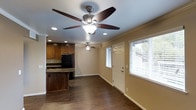 Located in San Diego, California, this single-story home offers a well-designed open-concept layout that seamlessly connects the living area and kitchen. The living space features rich, dark hardwood flooring that runs throughout, adding warmth and cohesion to the interior. Crown molding accents the ceilings, lending a refined architectural detail to the overall design. Ceiling fans with integrated lighting are installed in both the living area and kitchen, ensuring comfort and adequate illumination across the space. The kitchen is appointed with dark wood cabinetry, granite countertops, a kitchen island with bar seating, and black appliances, including a full-size refrigerator. Recessed lighting complements the ceiling fans, providing layered lighting options. Large windows fitted with horizontal blinds allow generous natural light to fill the interior while maintaining privacy. The front entry features a classic paneled white door, contributing to the home's clean and inviting aesthetic. The neutral wall tones throughout create a versatile backdrop that complements the dark flooring and cabinetry. Overall, the space presents a comfortable, functional, and well-appointed single-floor home in a desirable San Diego location.